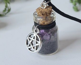 May include: A small glass bottle necklace with a cork stopper and a silver pentagram charm. The bottle is filled with black sand and purple crystals.