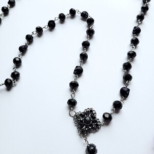 May include: A black beaded necklace with a silver skull charm and a black crystal pendant.