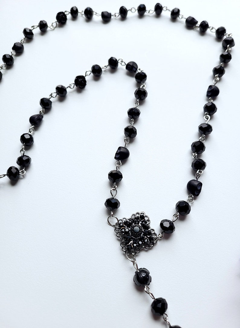 May include: A black beaded necklace with a silver skull charm and a black crystal pendant.