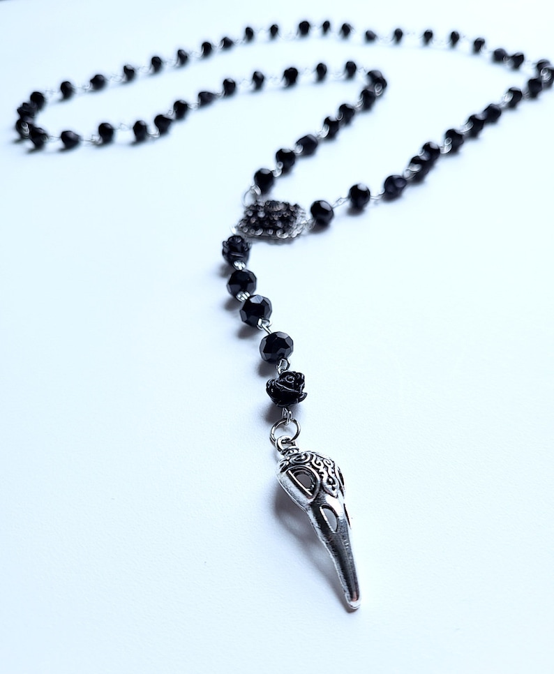 May include: Black beaded rosary necklace with a silver skull pendant and black rose accents.