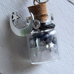 Sea Salt And Blue Sodalite Chips in a small Spell Bottle With Crescent Moon Charm Necklace laying on its side on white wooden surface.