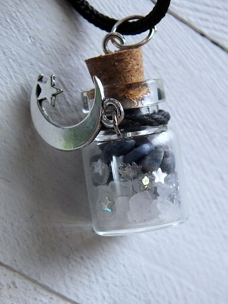 Sea Salt And Blue Sodalite Chips in a small Spell Bottle With Crescent Moon Charm Necklace laying on its side on white wooden surface.
