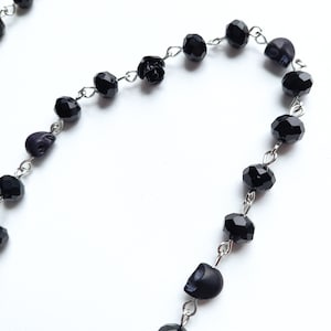 May include: A black beaded necklace with skull and rose charms. The necklace is made of silver chain and black beads.
