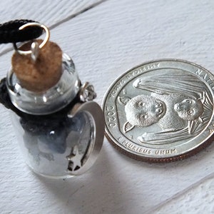 Sea Salt And Blue Sodalite Chips in a small Spell Bottle With Crescent Moon Charm Necklace on white wooden surface with a quarter next to it for size.