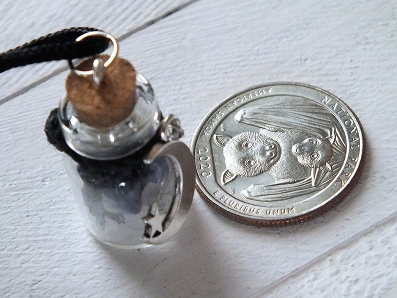 Sea Salt And Blue Sodalite Chips in a small Spell Bottle With Crescent Moon Charm Necklace on white wooden surface with a quarter next to it for size.