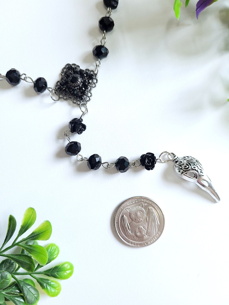 May include: Black beaded necklace with a silver skull charm and a silver filigree pendant. The necklace also features black rose accents.