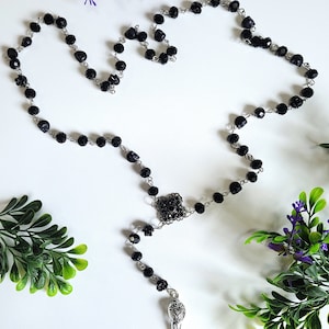May include: Black beaded rosary necklace with a silver crow pendant. The beads are faceted and the pendant has intricate details.