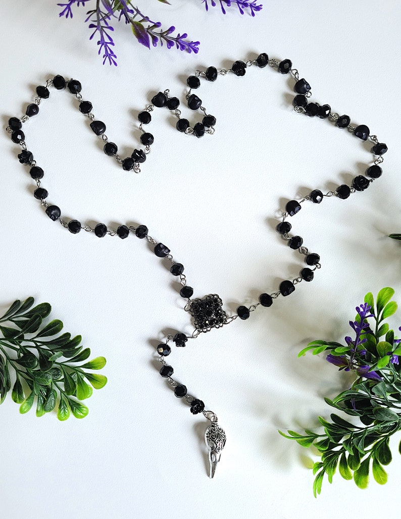 May include: Black beaded rosary necklace with a silver crow pendant. The beads are faceted and the pendant has intricate details.