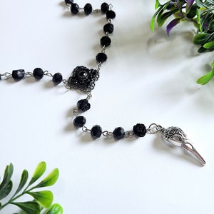 May include: Black beaded rosary necklace with a silver skull charm and a black flower accent.