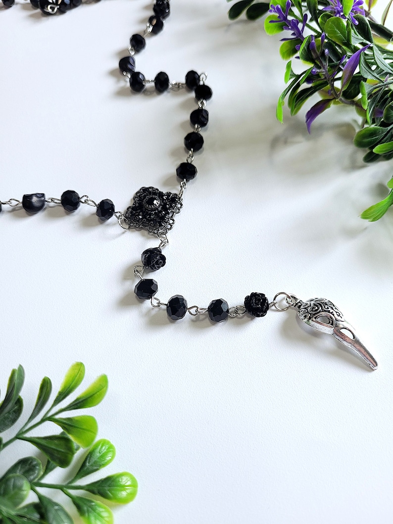 May include: Black beaded rosary necklace with a silver skull charm and a black flower accent.