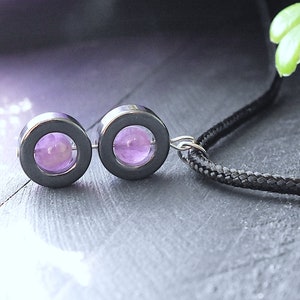 May include: A silver necklace with a black cord and two round pendants. Each pendant has a silver frame and a purple amethyst stone in the center.