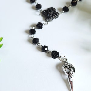 May include: Black beaded necklace with a silver skull pendant and black rose accents.