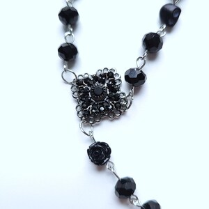 May include: Black beaded rosary necklace with a black rose charm and a silver centerpiece with black rhinestones.