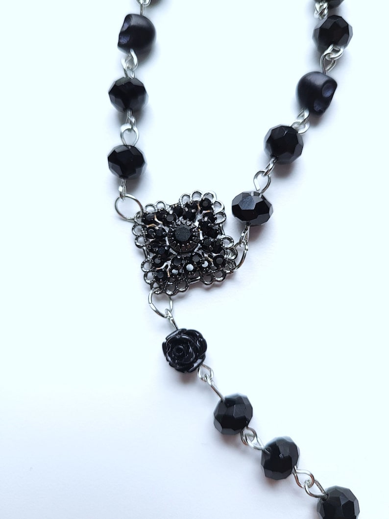 May include: Black beaded rosary necklace with a black rose charm and a silver centerpiece with black rhinestones.