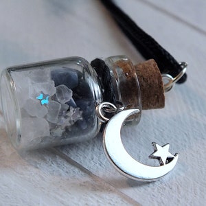 Sea Salt And Blue Sodalite Chips in a small Spell Bottle With Crescent Moon Charm Necklace laying on its side on white wooden surface.