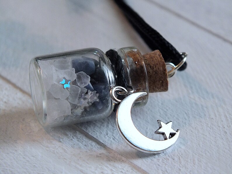 Sea Salt And Blue Sodalite Chips in a small Spell Bottle With Crescent Moon Charm Necklace laying on its side on white wooden surface.