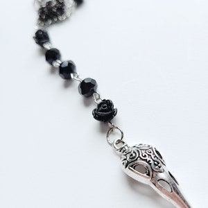 May include: A black beaded necklace with a silver crow skull pendant and a black rose charm.