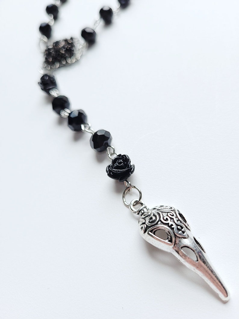 May include: A black beaded necklace with a silver crow skull pendant and a black rose charm.
