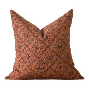 Könnte beinhalten: Ein quadratisches Dekokissen mit einem sich wiederholenden Batikmuster in Terrakotta-Orange und Dunkelanthrazit. Der Stoff zeigt ein dichtes, komplexes Design aus miteinander verbundenen floralen und geometrischen Motiven auf der gesamten Fläche.