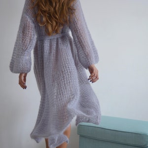 May include: A long, light purple knitted cardigan with a tie belt. The cardigan is made of a soft, fuzzy yarn and has a loose, flowing fit.