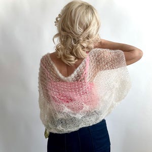 May include: A white knitted shawl with a delicate openwork pattern. The shawl is draped over a person's shoulders and is made of a soft, lightweight yarn.