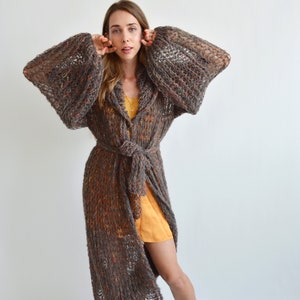 May include: A long, brown, knit cardigan with a tie belt and large sleeves. The cardigan has a loose, flowing fit and is made of a soft, textured yarn.