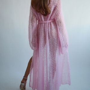 May include: A long, pink, knitted cardigan with a tie belt. The cardigan is made of a lightweight, airy fabric and has a loose, flowing fit.