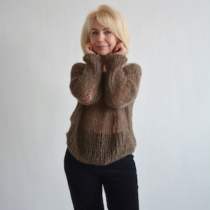 Peut inclure: Une femme portant un pull en tricot marron ample à maille ouverte délicate. Elle porte un pantalon noir.