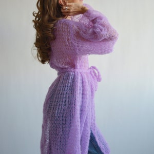 May include: A long, light purple knitted cardigan with a tie belt. The cardigan is made of a loose, open knit fabric.