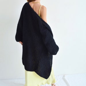 Op de afbeelding: Een zwarte, lange, gebreide cardigan met een losse pasvorm en een licht oversized silhouet. De cardigan is gemaakt van zacht, dik garen en heeft een ontspannen, casual stijl.