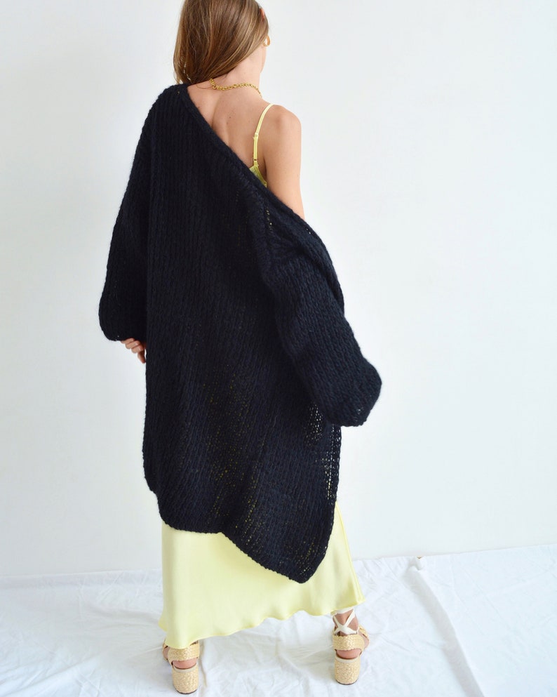 Op de afbeelding: Een zwarte, lange, gebreide cardigan met een losse pasvorm en een licht oversized silhouet. De cardigan is gemaakt van zacht, dik garen en heeft een ontspannen, casual stijl.