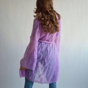 May include: A long, light purple knitted cardigan with a tie belt. The cardigan is made of a delicate, open-weave fabric.