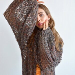 May include: A brown, open knit cardigan with a loose fit and long sleeves. The cardigan has a subtle orange and yellow fleck throughout the fabric.
