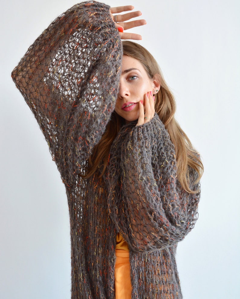 May include: A brown, open knit cardigan with a loose fit and long sleeves. The cardigan has a subtle orange and yellow fleck throughout the fabric.