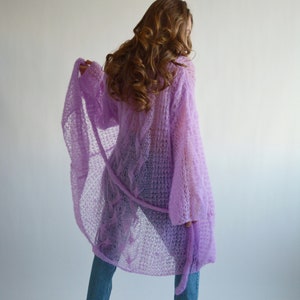 May include: A light purple knitted cardigan with a loose fit and long sleeves. The cardigan is made of a delicate, open-weave fabric and has a tie at the waist.