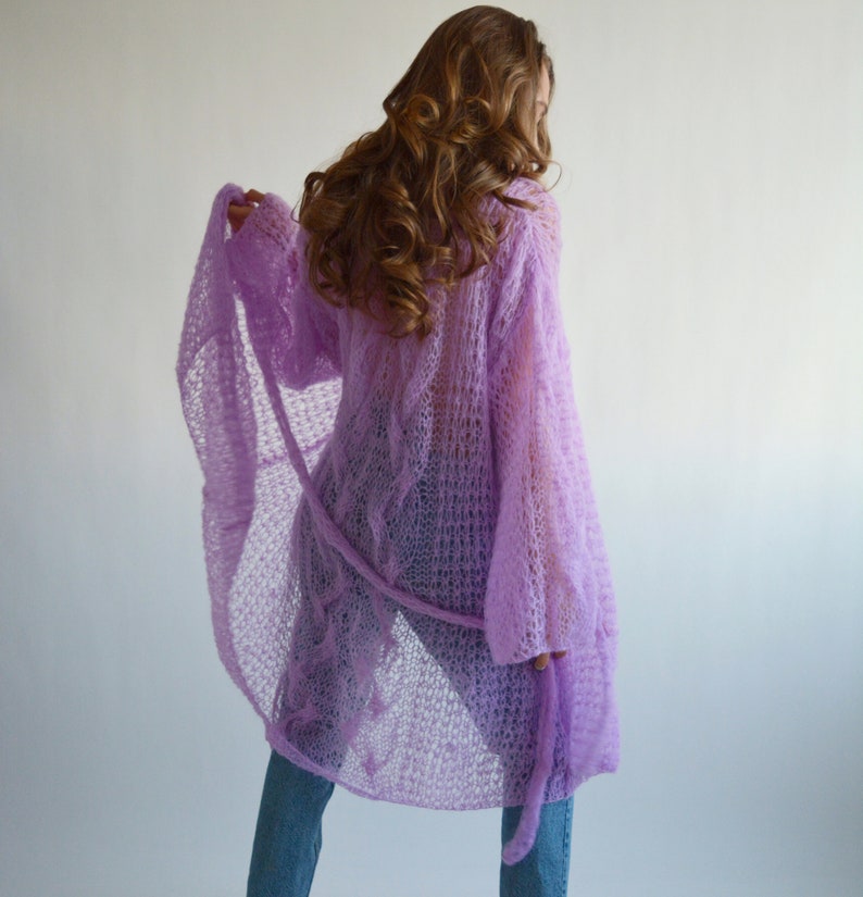May include: A light purple knitted cardigan with a loose fit and long sleeves. The cardigan is made of a delicate, open-weave fabric and has a tie at the waist.