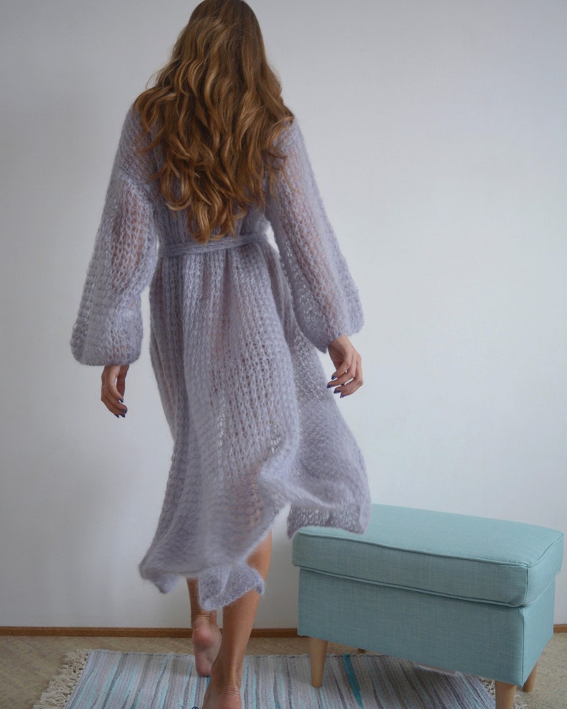 May include: A long, light purple knitted cardigan with a tie belt. The cardigan is made of a soft, fuzzy yarn and has a loose, flowing fit.