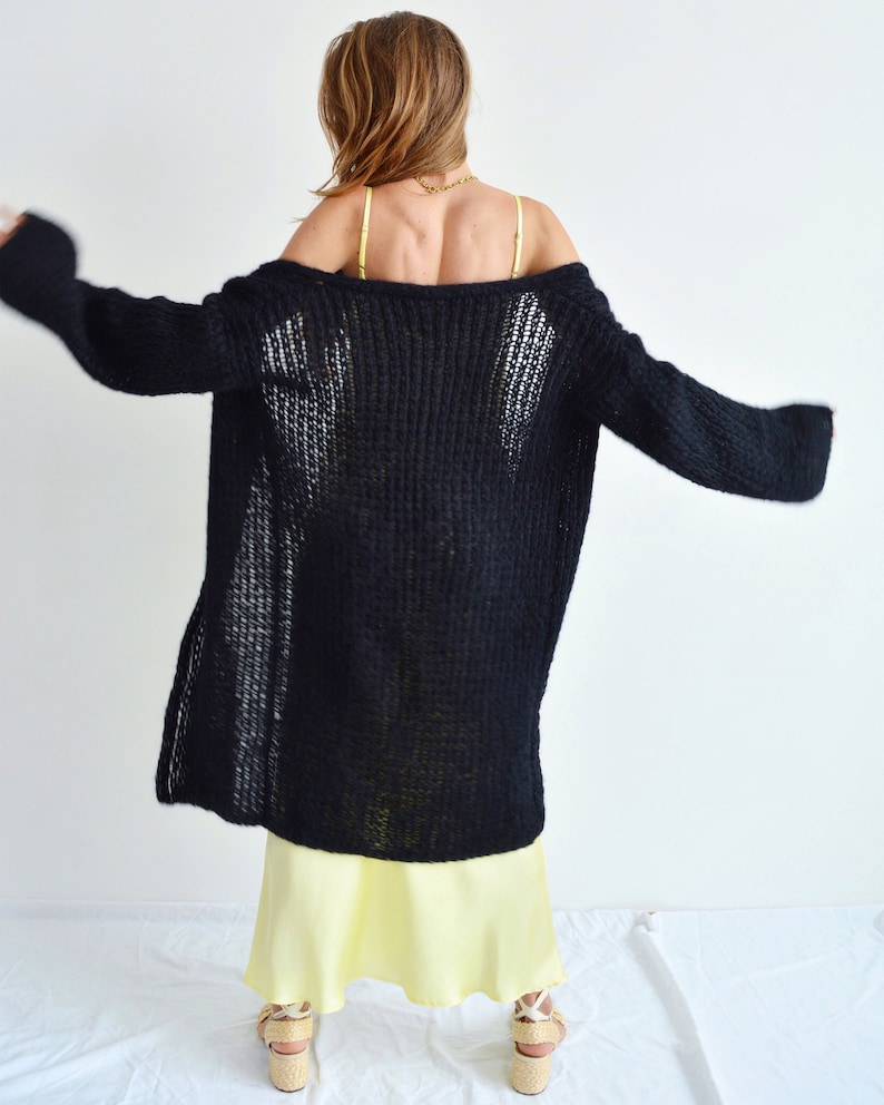Op de afbeelding: Een zwarte, langarmige gebreide cardigan met een losse pasvorm en een diepe V-hals. De cardigan is gemaakt van zacht, lichtgewicht garen en heeft een ontspannen, casual stijl.