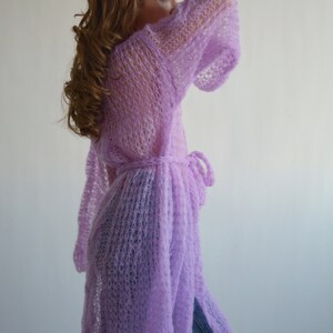 May include: A long, light purple knitted cardigan with a tie belt. The cardigan is made of a loose, open weave and has a relaxed fit.