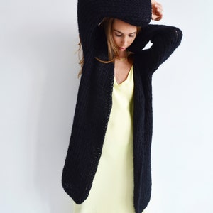 Op de afbeelding: Een zwarte gebreide cardigan met een lange, losse pasvorm. De cardigan is open aan de voorkant en heeft een ontspannen, casual stijl.