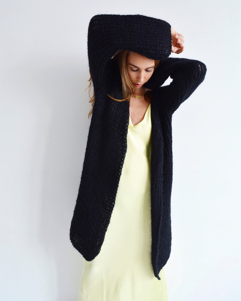 Op de afbeelding: Een zwarte gebreide cardigan met een lange, losse pasvorm. De cardigan is open aan de voorkant en heeft een ontspannen, casual stijl.