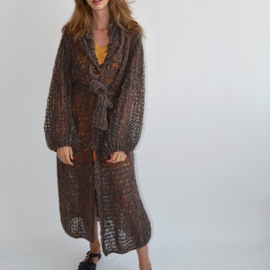 May include: A long, brown, knit cardigan with a tie belt and a button closure. The cardigan has a loose fit and is made of a soft, lightweight yarn.