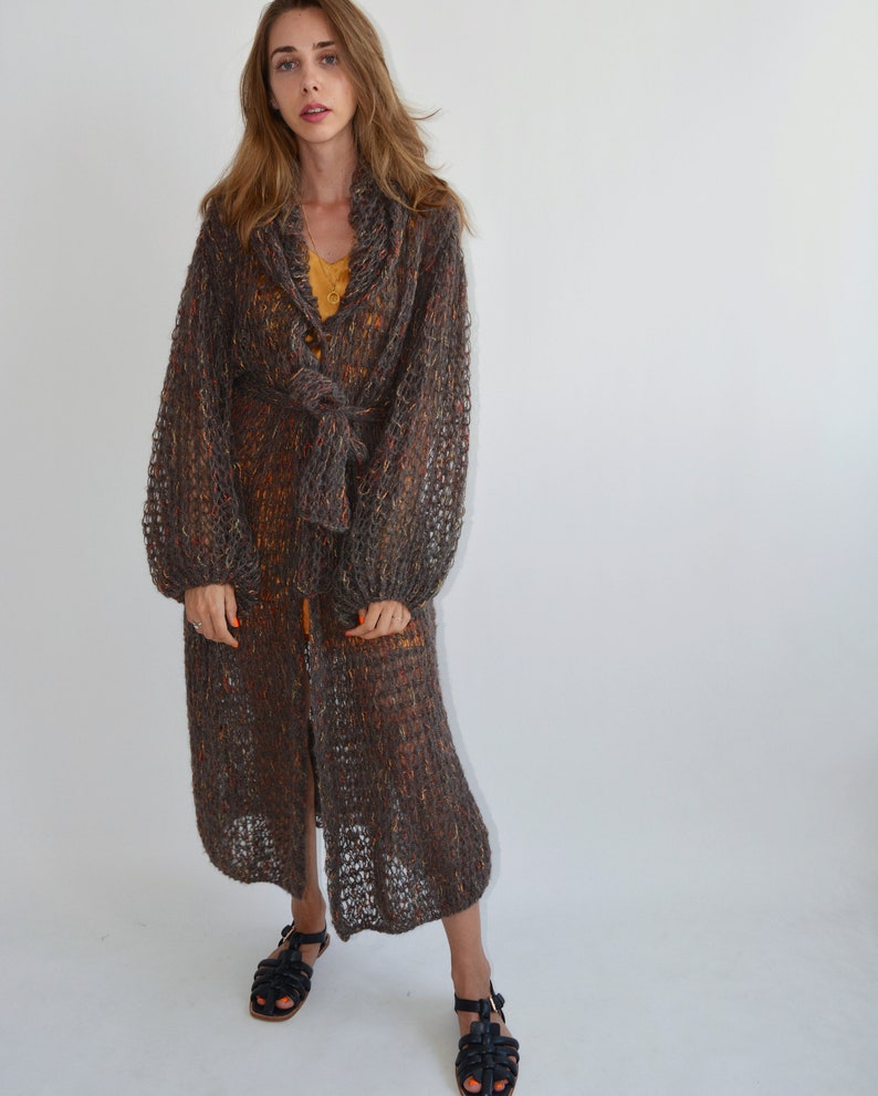 May include: A long, brown, knit cardigan with a tie belt and a button closure. The cardigan has a loose fit and is made of a soft, lightweight yarn.