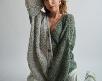 May include: A woman wearing a green and white knitted cardigan with a button fastening. The cardigan is made of a soft, fluffy material. The woman is wearing light green trousers.