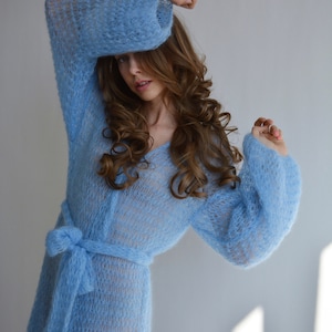 Peut inclure: Une robe en tricot bleu clair à manches longues et une ceinture à nouer. La robe est faite d'un tissu doux et aéré et a une coupe ample et fluide.
