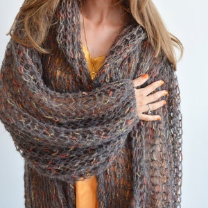 May include: A brown, orange, and gray knitted cardigan with a loose, open weave. The cardigan is worn open and has a long, flowing style.