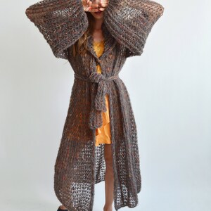 May include: A long, brown, knitted cardigan with a tie belt and large sleeves. The cardigan is made of a loose, open weave and has a slightly textured look.