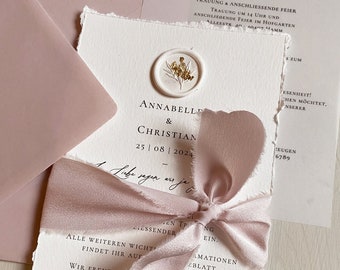 May include: A white wedding invitation with a pink ribbon and a wax seal with a floral design. The invitation reads "Annabelle & Christian 25|08|2024".