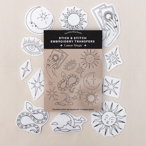 May include: A set of stick and stitch embroidery transfers titled Lunar Magic, featuring black line art designs of suns, moons, stars, snakes, eyes, and hands holding tarot cards on a tan paper backing, surrounded by individual cut-out stickers.