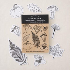 Puede incluir: Un conjunto de transferencias para bordar Stick & Stitch titulado Autumn Harvest, que incluye un paquete de papel marrón con dibujos lineales negros de setas, hojas, bellotas y una calabaza, rodeado de pegatinas individuales con los mismos diseños.